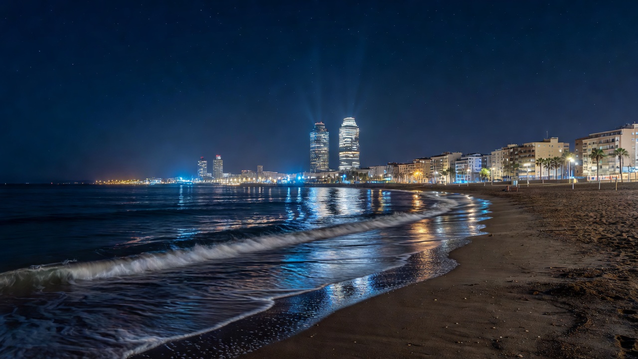 Barcelona coastal skyline along Barceloneta beach and Port Olimpic with ocean waves at night